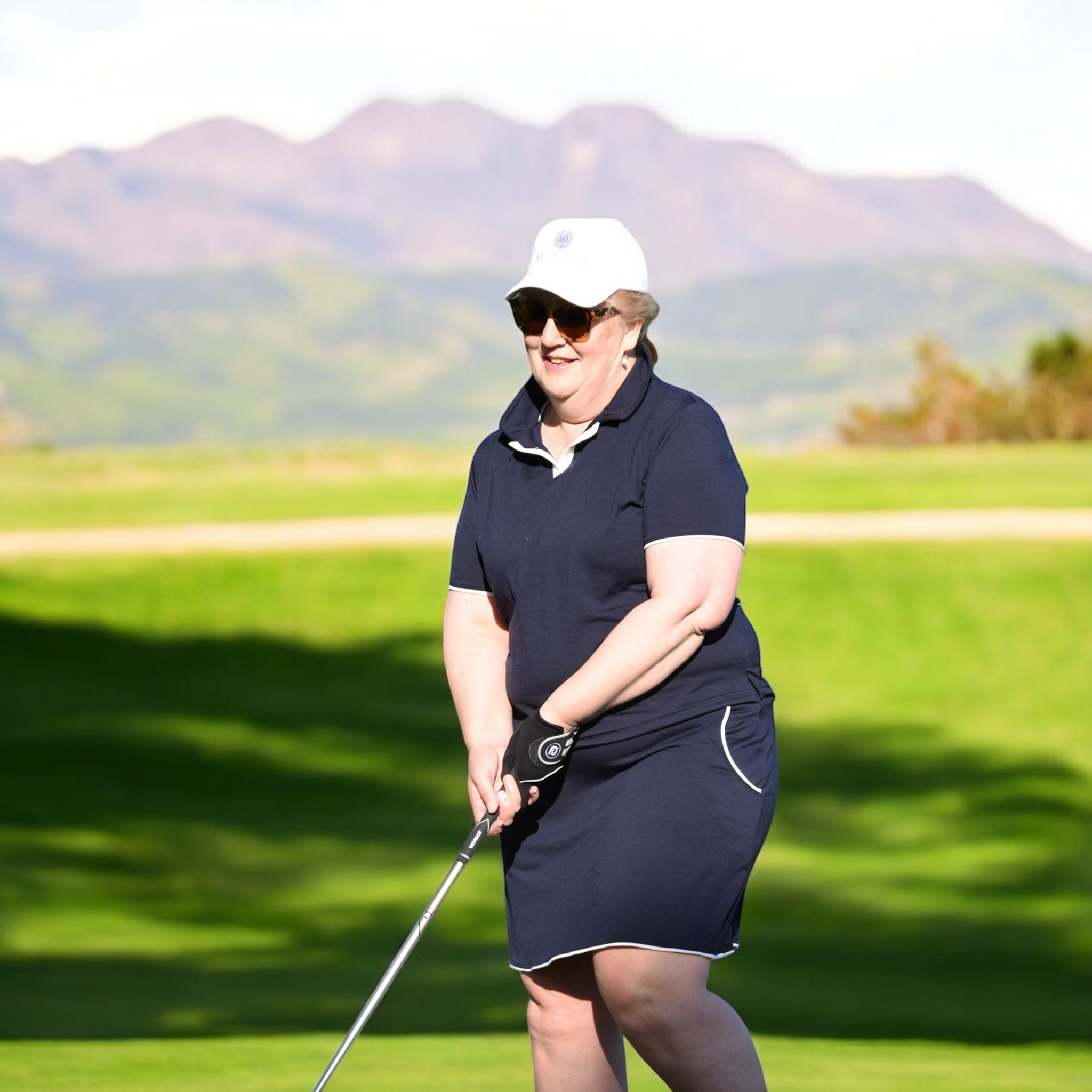 Ladies Merino Golf Skirt - Navy worn by smiling woman playing golf on sunny course with mountains in background